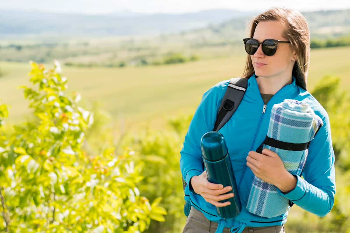 Girl with sunglasses holding a water bottle and a blanket.