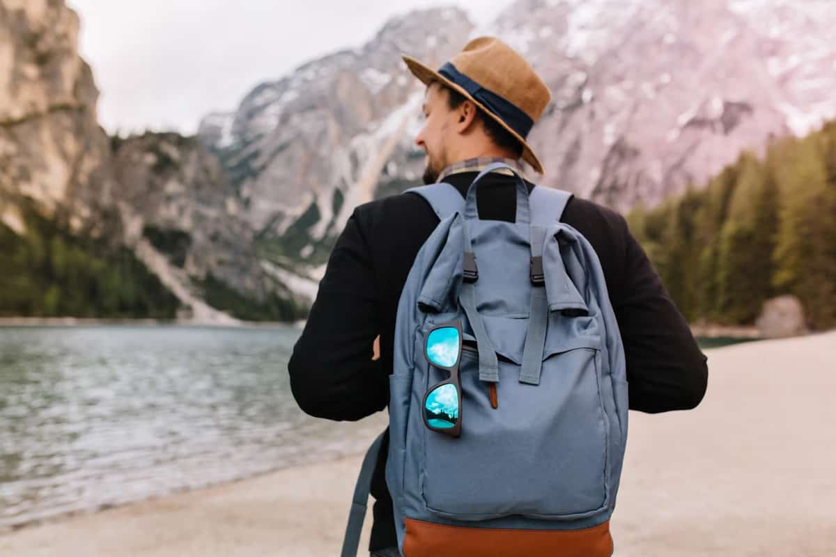 Back view of a man with a backpack, near a river in mountains.