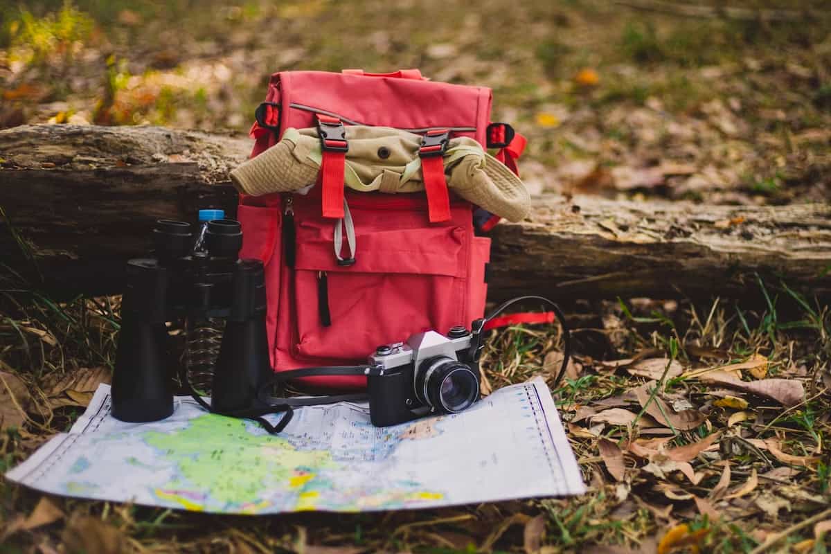 Red backpack in a forest with the essential items for a budget nature walks.