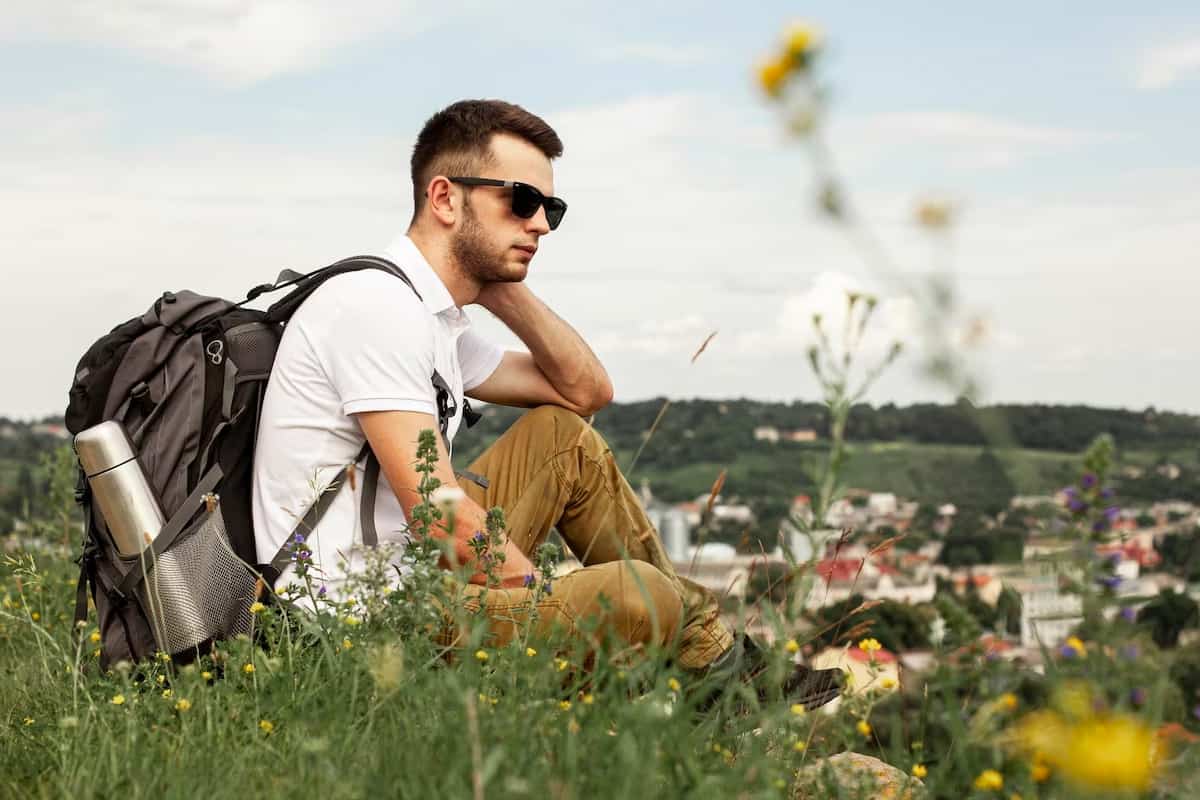 A man with a backpack is siting on the grass with flowers.