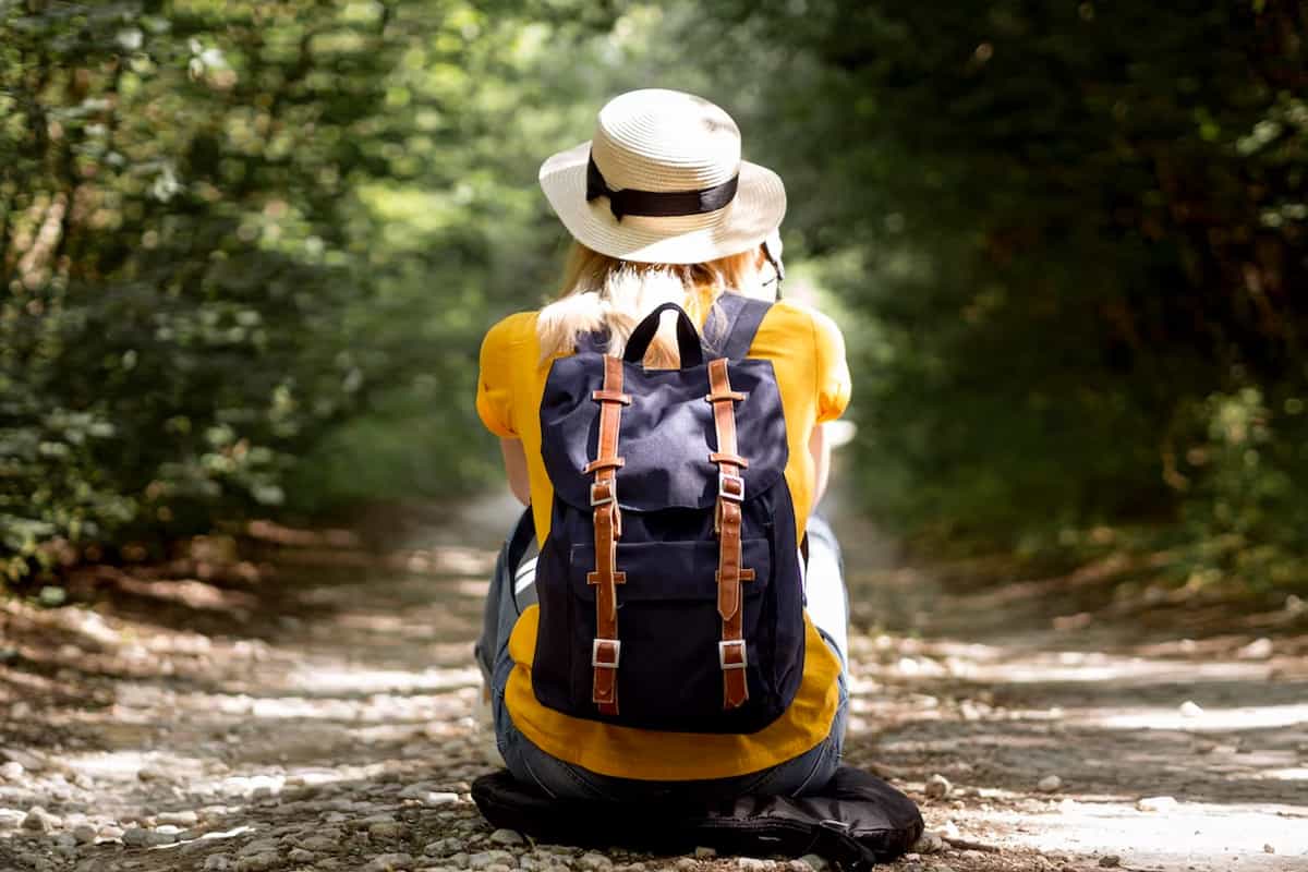 Back view of a girl with backpack sitting in the ground in the forest.