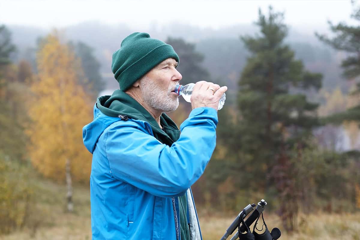 A man drinking a bottle of water in nature.